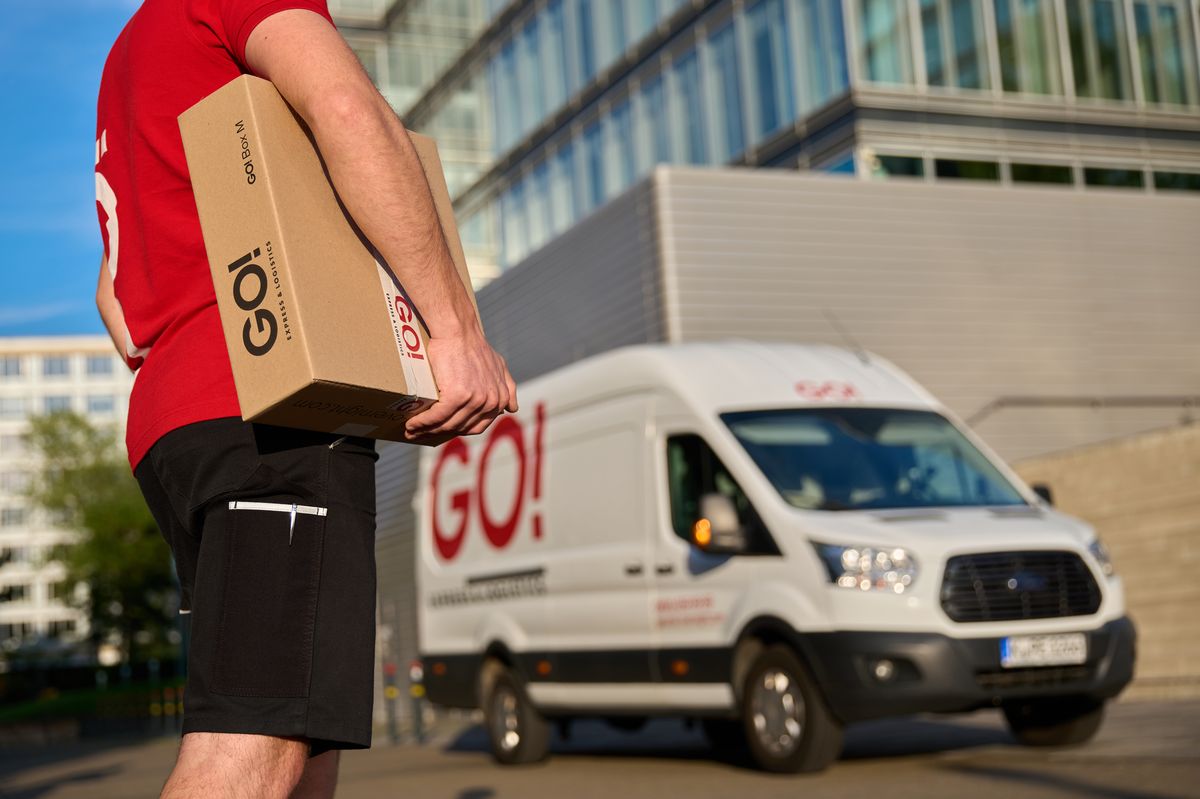 GO!-Kurier mit Paket vor einem GO!-Transporter